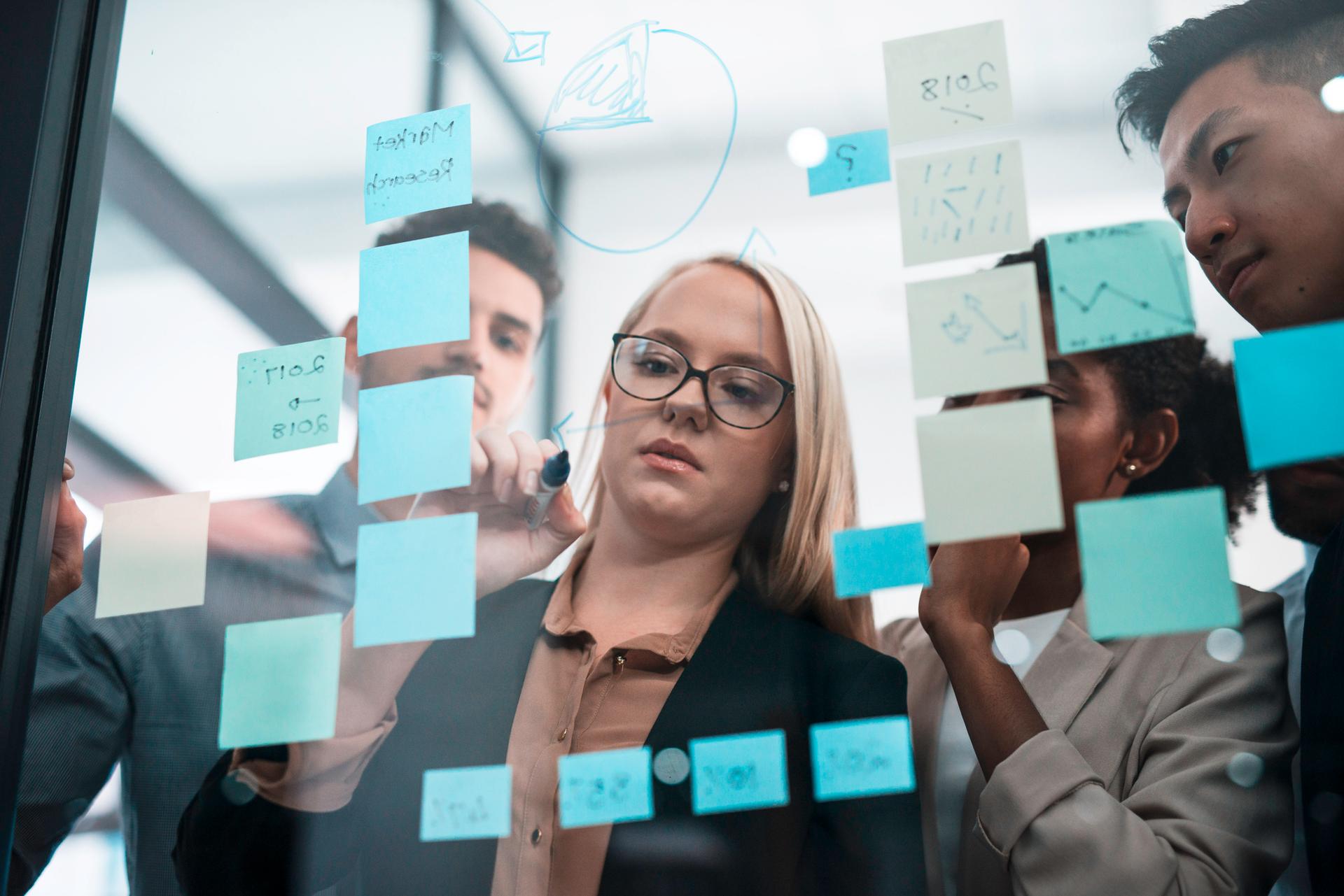 Team Collaborating in an Office Using Sticky Notes on Glass Panel for Business Planning