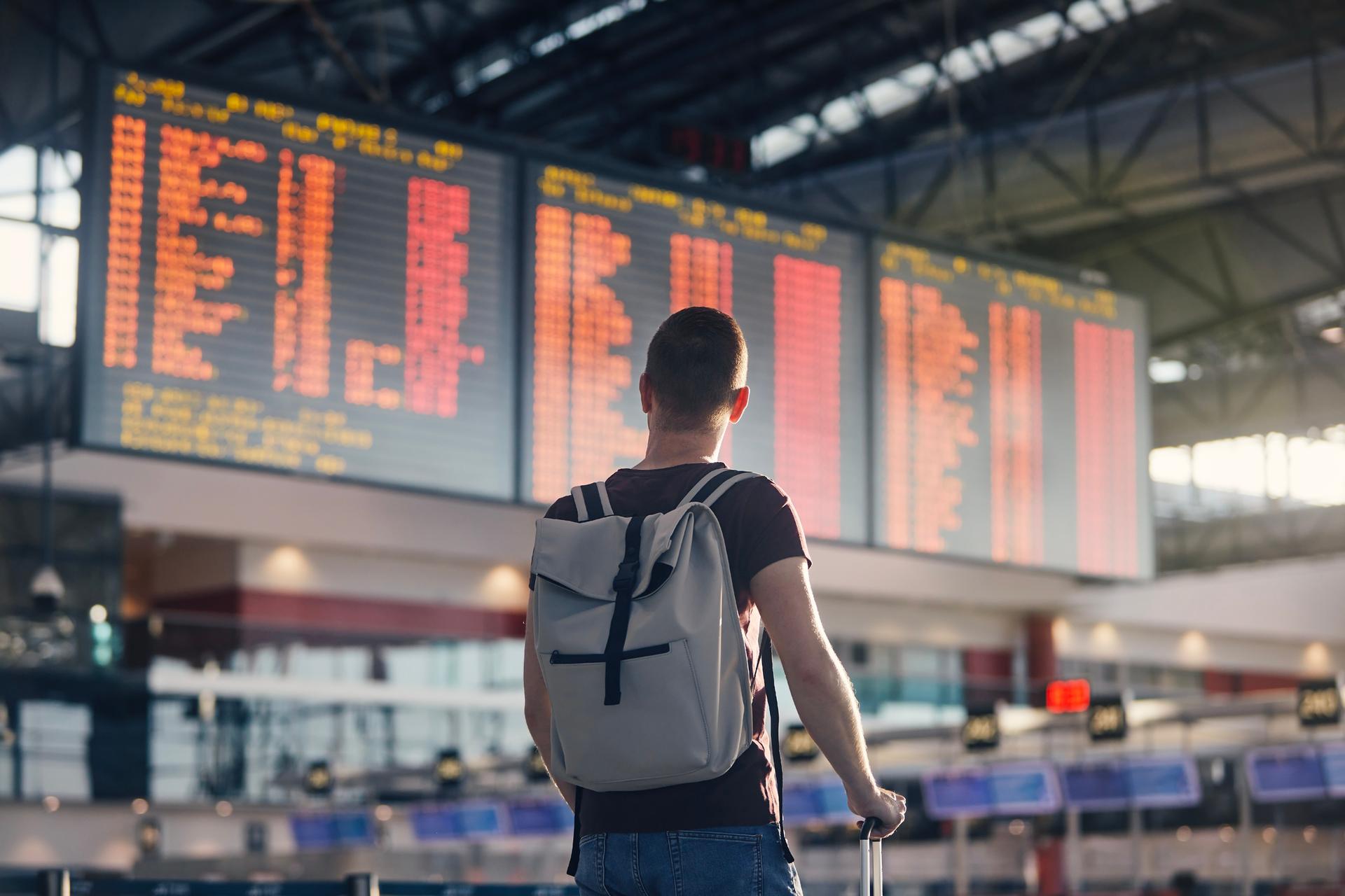 Man walking with backpack and suitcase walking through airport terminal